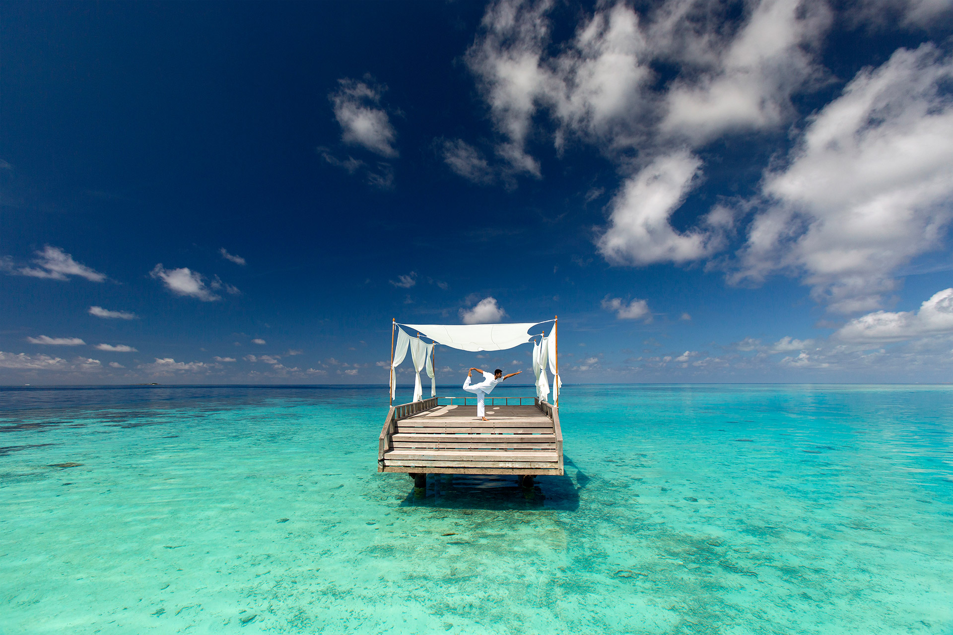 Mann macht Yoga auf Holzplattform im Meer
